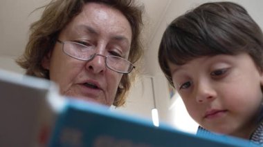 Büyükannesi torununa kitap okuyor, her ikisi de hikayeye derinden odaklanmış. Aile bağının, öğrenmenin ve paylaşılan okuma anlarıyla özel bağlantının özü