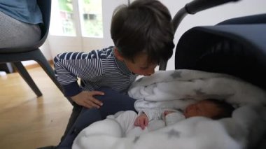 Küçük çocuk, yeni doğmuş kardeşini öpmek için araba koltuğunda uyuyor. O hassas an, ev ortamında kardeşler arasındaki sevgi ve bağı yakalar.