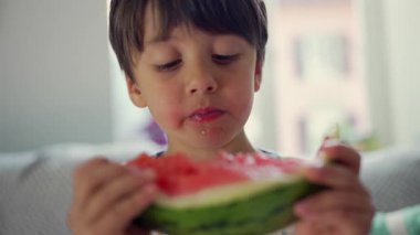 Çocuk elinde büyük bir dilim karpuz, yakın çekim, yaz atıştırması, sağlıklı beslenme, taze ve sulu meyve, evde rahat bir an, doğal ışık, çocuk