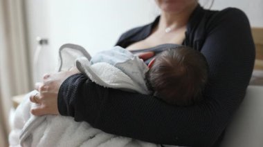 Anne yeni doğmuş bebeği emziriyor, yumuşak bir battaniyeye sarılıp anne ve çocuk arasındaki yakın ve besleyici bir annelik anını yakalıyor.