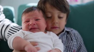 Küçük bir çocuk ağlayan yeni doğan bir kardeşi rahatlatıyor, sıcak bir yuvadaki kardeşler arasındaki koruyucu ve sevgi dolu bağı gösteriyor.