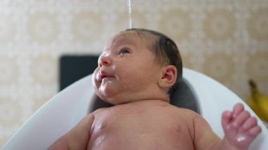 Yeni doğmuş bebek banyo sırasında küvette yatıyor, bebek ifadesine ve etkileşimine odaklanıyor, hassas anları vurguluyor.