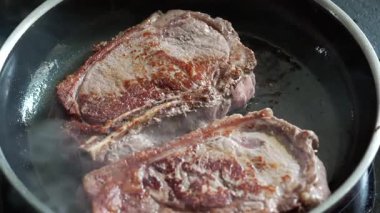 Sıcak tavada pişen biftekler, kahverengileşmeye başlıyor, taze sığır eti, cızırtılı ses, ev mutfağı, mutfak hazırlığı, lezzetli bir yemek hazırlama, pişirme sürecinin detaylı görüntüsü.