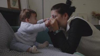 Anne bebekle kanepede iletişim kuruyor, şakacı yüz yüze iletişim kuruyor, erken çocukluk gelişiminde neşe ve bağlılık gösteriyor, ev ortamını büyütüyor.