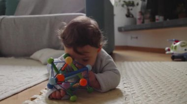 Bebek paspasın üzerinde renkli oyuncaklarla oynuyor, dokunsal keşif ve oyun yoluyla hareketli beceriler geliştiriyor, güvenli bir ev ortamında odaklanma ve bağlılık gösteriyor