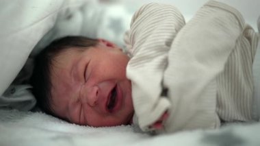 Yeni doğmuş bebek yatakta ağlıyor, hassas ve duygusal bir an yaşıyor. Bebeğin yüzü, erken yaşların hassasiyetini ve hassasiyetini vurgulayarak, sıkıntılı bir ifade sergiliyor.