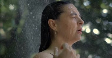 Açık hava duşunun altında kadının yakın çekimi, yavaş çekimde su aşağı akıyor 800 fps, gözler kapalı, doğada huzurlu bir an, yaz serinlemesi