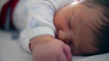 Yeni doğan bebek huzur içinde uyuyor, yüzünde ve elinde yakın planla, çocukluk döneminin huzurlu ve narin doğasını yakalıyor..