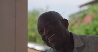 Afrika kökenli yaşlı bir adam neşeyle gülüyor, başını arkaya eğiyor, açık havada canlı bir yeşillikle, coşkulu bir mutluluk, kendine güven ve sıcak bir kişilikle.