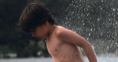 Su sıçratma sahnesinde oynayan bir çocuk, bir yaz günü neşeli ve ferahlatıcı deneyimi vurguluyor, 800 fps 'de yavaş çekim yakalanıyor.