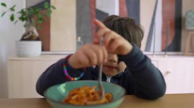 Yoğun odaklı bir çatal üzerinde spagetti çeviren küçük çocuk, sıcak bir ev ortamında yemek saatinde konsantrasyon ve kararlılık gösteriyor.