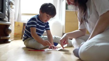 Anne ve oğul yerde eğlenceli ve yaratıcı bir aktivite içinde. Parlak ve neşeli bir ev ortamında odaklanma ve etkileşimle dolu bir anı paylaşıyorlar..