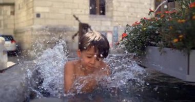 Genç bir çocuk suya atlıyor, çiçeklerle çevrili bir çeşmeye neşeyle sıçrıyor, tarihi bir Avrupa şehir meydanında, 800 fps hızla süper yavaş çekimde yakalandı..