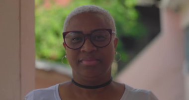 Latin kökenli, kısa beyaz saçlı, gözlüklü, sakin ve kendinden emin, canlı ve doğal bir şekilde dışarı bakan Latin bir kadın.