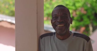 Olgun bir adam açık havada bir sütuna yaslanıyor, sıcak bir şekilde gülümsüyor, neşe ve orijinallik sergiliyor, Afrika etnik kökeni, yakın bakış açısı
