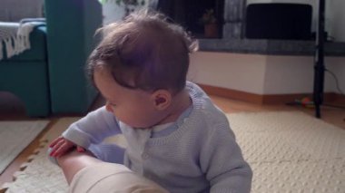 Bebek, anne bacağının üzerinde tuhaf bir ifadeyle dinleniyor, evde aile bağlarını kurma zamanı, bebek ve anne arasında oyuncu ve besleyici bir an, dokunsal bir merakla dünyayı keşfediyor.