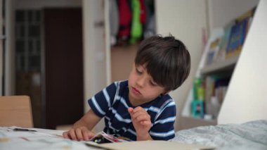 Küçük bir çocuk, yatağında kitap ve oyuncaklarla dolu bir odada yalnız oyun ve odaklanma anının altını çizerek, küçük bir oyuncakla ya da yapbozla derinden meşgul.