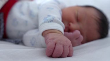 Yeni doğmuş bebek bir eliyle bir yatakta uzanıyor. Yüzünün yanında dinleniyor. Huzur içinde uyuyor. Yavruların yumuşak, nazik ifadeleri bir anlık sakinlik ve güven gösteriyor.