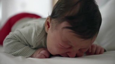 Yeni doğmuş bebek, çizgili tulum giymiş bir şekilde yatağa uzanmış ağlarken, erken yaştaki çocukların doğal mücadelelerini ve ilgi ve ilgiye duyma ihtiyacını vurguluyor.