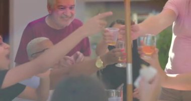 Arkadaşlar açık hava kutlamalarında içkilerle kadeh kaldırıyor, güneşin altında çeşitli kültürlerde kahkaha, bağlantı ve neşe dolu enerjilerini paylaşıyorlar.