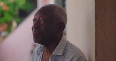 Sakin bir ifadeyle Afrika kökenli yaşlı bir adam, düşünceli bir şekilde yan tarafa bakıyor, açık havada yumuşak doğal ışık ve canlı yeşillikle, bilgelik ve dinginlik yayıyor.