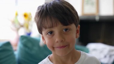 Yumuşak gülüşlü, sıcak yüzlü, doğrudan göz teması kuran, çocukluk masumiyeti, doğal görünüş, rahat ev ortamları olan genç bir çocuğun yakın plan portresi.