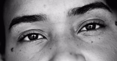 Tek renkli, siyah beyaz kameraya bakan genç bir siyahi kadının yoğun makro-yakın çekim yüzü.