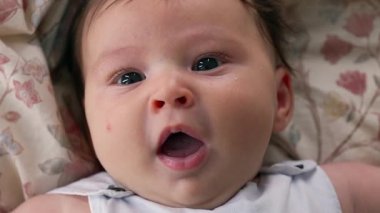 Bebek battaniyeye uzanmış, sakin bir ifadeyle doğrudan kameraya bakıyor. Bebek yüz hatlarına odaklanıyoruz. Bir masumiyet ve sükunet anı yakalıyoruz..