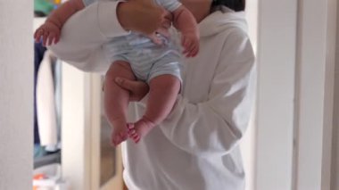 Anne bebeğini kaldırıyor ve bebek yanağını öpüyor. Onu güvenli bir şekilde evin koridorunda tutuyor. Bebek merakla ve hareketle dışarı bakar..