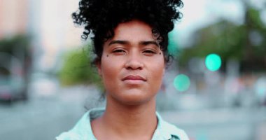 Genç siyah Latin bir kadın ciddi ciddi kameraya bakıyor. Arka planda Afrika kökenli 20 'li yaşların portresi