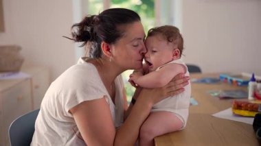 Anne, bebeğin yanağını öpüyor, sevgi dolu kucaklıyor, sevgi dolu bir bağ kuruyor, aile içi yakınlık kuruyor, özel bir bağ kuruyor, sevgi dolu bir ilişki kuruyor, sıcak bir yuva kuruyor..