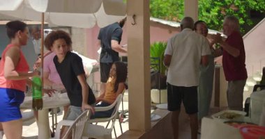 Çeşitli aile ve arkadaşlar açık havada yemek yiyip kaynaşıyor, sıcak bağlantıların ve günlük bir öğle yemeği sırasında hareketli bir atmosferin tadını çıkarıyorlar.