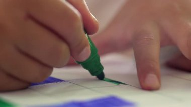 Genç bir çocuğun elinde yeşil bir işaret, bir ızgara içinde dikkatlice boyama, barışçıl bir sanat etkinliği sırasında hassasiyet, odak ve yaratıcılık gösteren yakın plan..