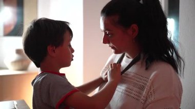 Anne ve oğul evlerinde samimi bir anı paylaşıyorlar. Çocuğun annesinin kolyesini gözünün içine bakarak tutması, aile bağı ve duygusal bağ..