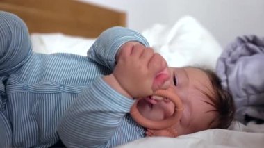Bebek yatakta uzanıyor, iki eliyle diş çıkarma yüzüğünü kavrıyor, nesneyi keşfediyor, motor becerilerini geliştiriyor, duyusal keşifler, çiğneme oyuncakları, çocukluk merakı, ev dekorasyonu.