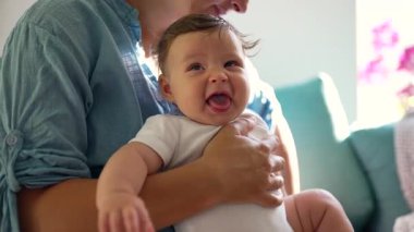 Anne hapşırık sırasında bebeği kucağına alır, bebek buruşuk yüzle tepki verir, doğal refleks anı, erken çocukluk gelişimi, bakım, sıcak bir evde aile sıcaklığı.