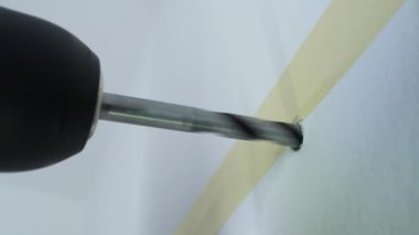 Duvarda bir delik açan matkabın yakın plan çekimi, kesin bir ev geliştirme sürecini gösteriyor, delme işlemindeki detaylara dikkat ederek ve bandı doğruluk için kullanarak..