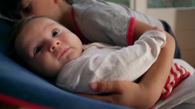 Büyük kardeş bebeği sıkıca tutuyor, güçlü kardeş kucaklıyor, koruyucu ama ezici, çocukluk yakınlığı, aile bağı, şefkat anı, duygusal bağ