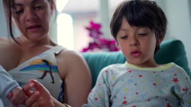 Bir anne bebeğini emzirirken, büyük çocuk da rahat bir yuva ortamında kitap okumaya odaklanıyor..