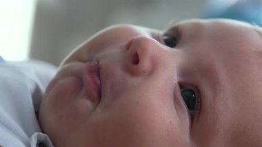 Bebek suratlı, ağzı açık ve neşeli bir yüz ifadesi olan birinin yakın çekimi. Bebek yatağa uzanıyor, yukarıya bakıyor, narin özelliklerindeki masumiyet ve mutluluğu vurguluyor..