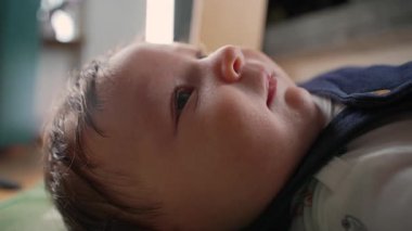 Bebek paspasın üzerinde uzanıyor, sıcak bir evde nazik bir ifadeyle yukarıya bakıyor. Çocuk rahat ve rahat görünüyor, sakin ve sakin atmosfer