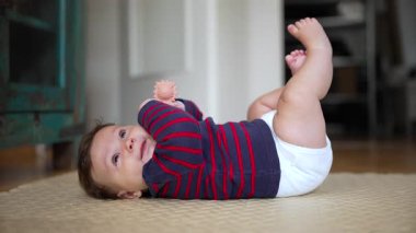 Bebek yerde yuvarlanıyor, hareketle meşgul oluyor, erken motor beceri gelişimi, neşeli an, vücut koordinasyonunu keşfetmek, bebek büyümesi, merak, keşif