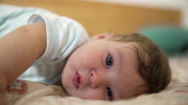 Yatakta uzanan bebek, kameraya merakla bakıyor, gevşemiş ve dikkatli bir ifade, erken çocukluk keşfi, sıcak ve huzurlu bir yuva.