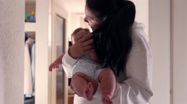 Bebek annesinin saçını çekerken, o da nazikçe minicik elini koparmaya çalışıyor. Ev koridorunda ebeveynliğin zorluklarını yakalayan samimi bir annelik anı..