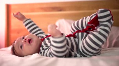 Aktif bebek yatakta yuvarlanıyor, kollarını ve bacaklarını oynatıyor, rahat bir ev ortamında hareket ve koordinasyonu keşfediyor.