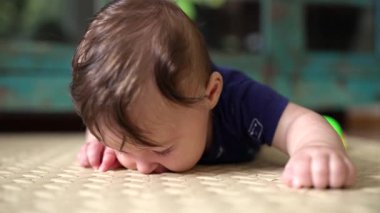 Bebek mindere uzanıyor, yüzü bastırılmış, dokuyu keşfediyor, erken çocukluk merakı, duyusal keşif, motor geliştirme, bebek oyun zamanı, dokunarak öğrenme