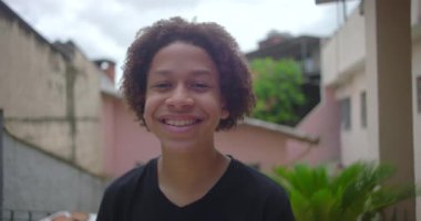 Latin Amerika 'nın yerleşim bölgesinde sıcak bir şekilde gülümseyen, neşeli bir ortama mutluluk ve gençlik güveni saçan Afrika kökenli Latin kökenli genç çocuk.