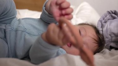 Yatakta uzanmış bebek, elinde diş çıkarma yüzüğü, ağızla nesneyi keşfetmek, erken duyusal gelişim, çiğneme oyuncağı, sakız, bebek oyunu, sakinleştirme anı, yuva kurma