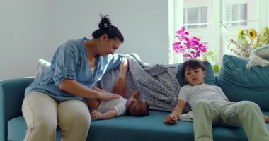 Bir annenin bebeğiyle nazikçe etkileşime girdiği yakın plan bir kanepede oğlunun yanında dinlendiği sıcak aile anı.