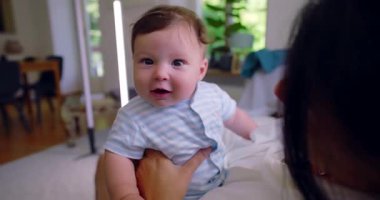 Bebeğin doğrudan kameraya baktığı yakın çekim. Bu sırada anne, bebeği sevgi dolu bir şekilde sakin bir evde tutarak anne-baba ve çocuk arasındaki huzurlu ve samimi sahneyi yakalıyor.